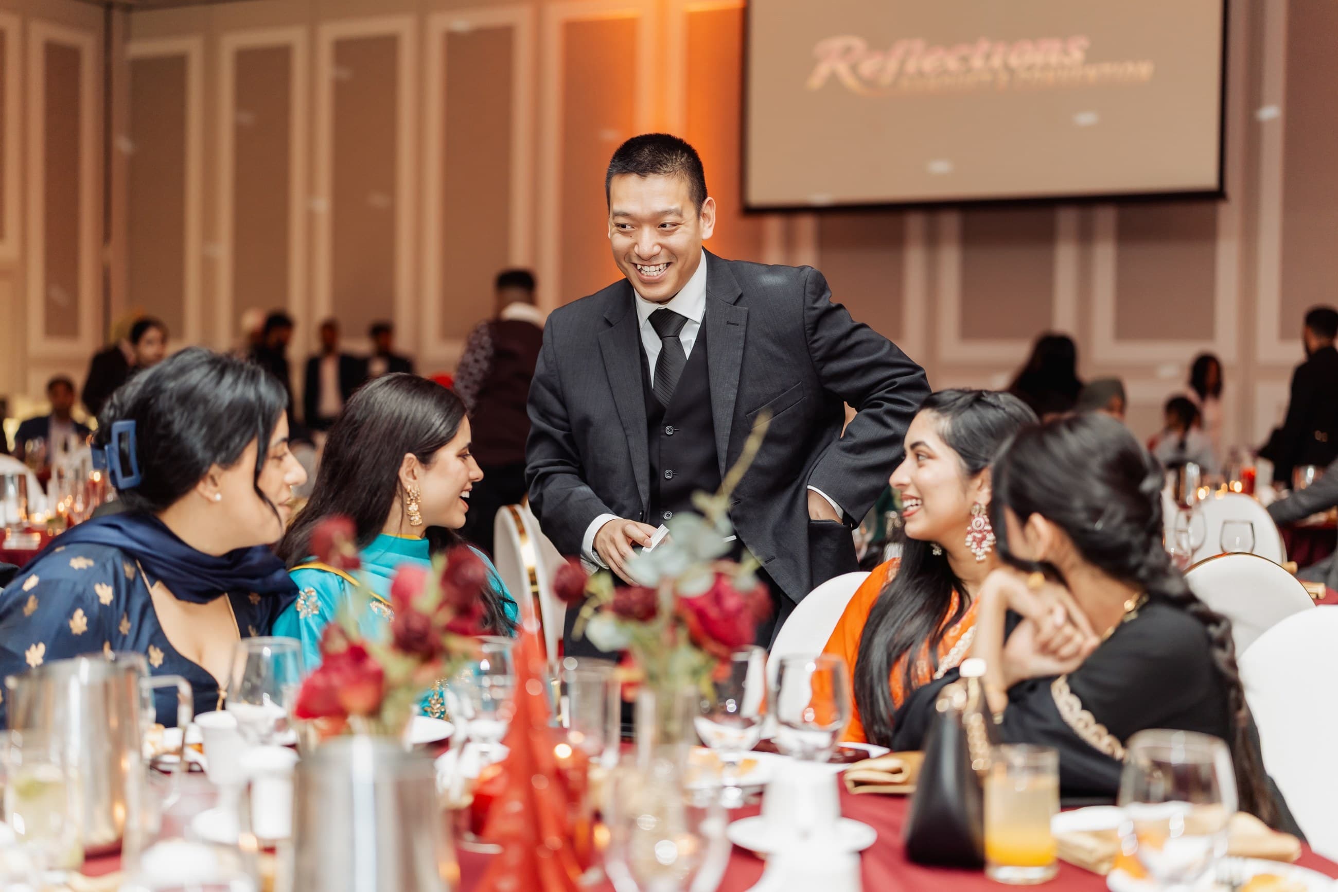 John Ha smiling with wedding reception guests during interactive close-up magic at a decorated table