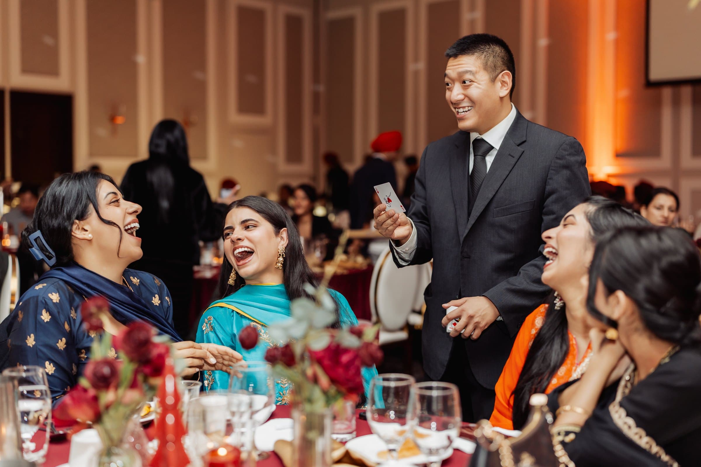 John Ha performing close-up magic at a holiday party table with guests laughing